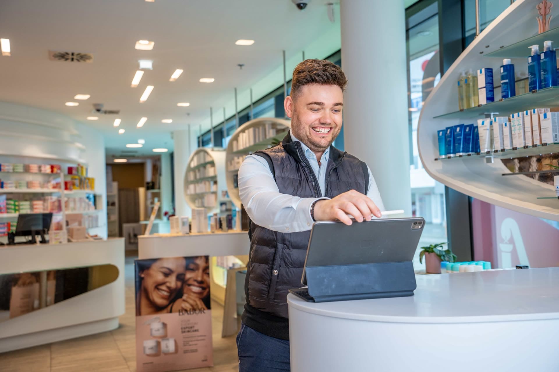 Apotheker am Beratungstresen vor den Regalen einer Apotheke.